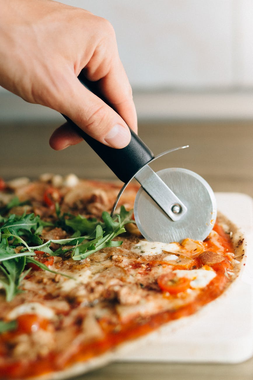 person holding black handled knife slicing pizza